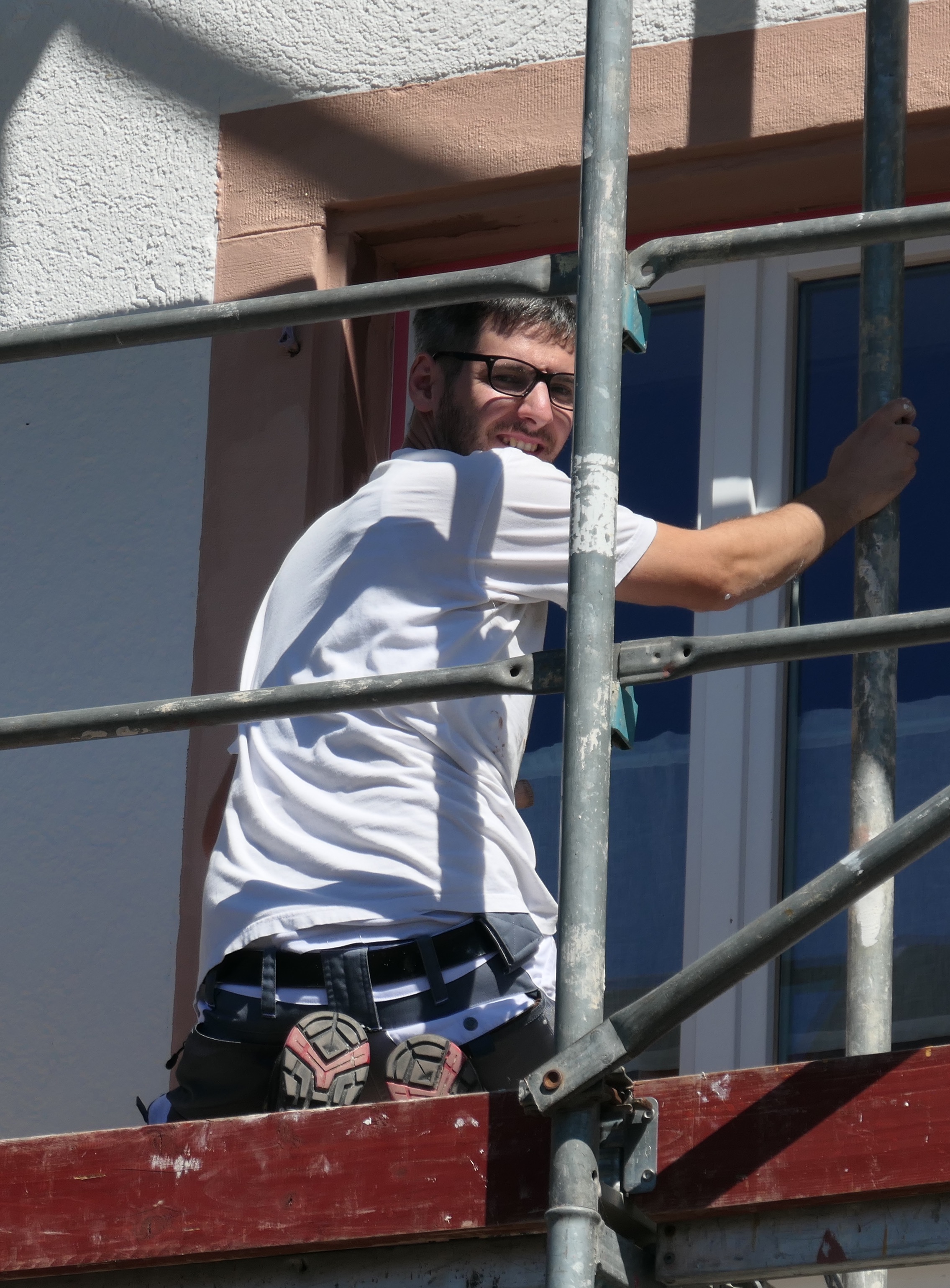 Malermeister Fabian Räuber sitzt auf einem Gerüst an einer Wohnhaus-Fassade